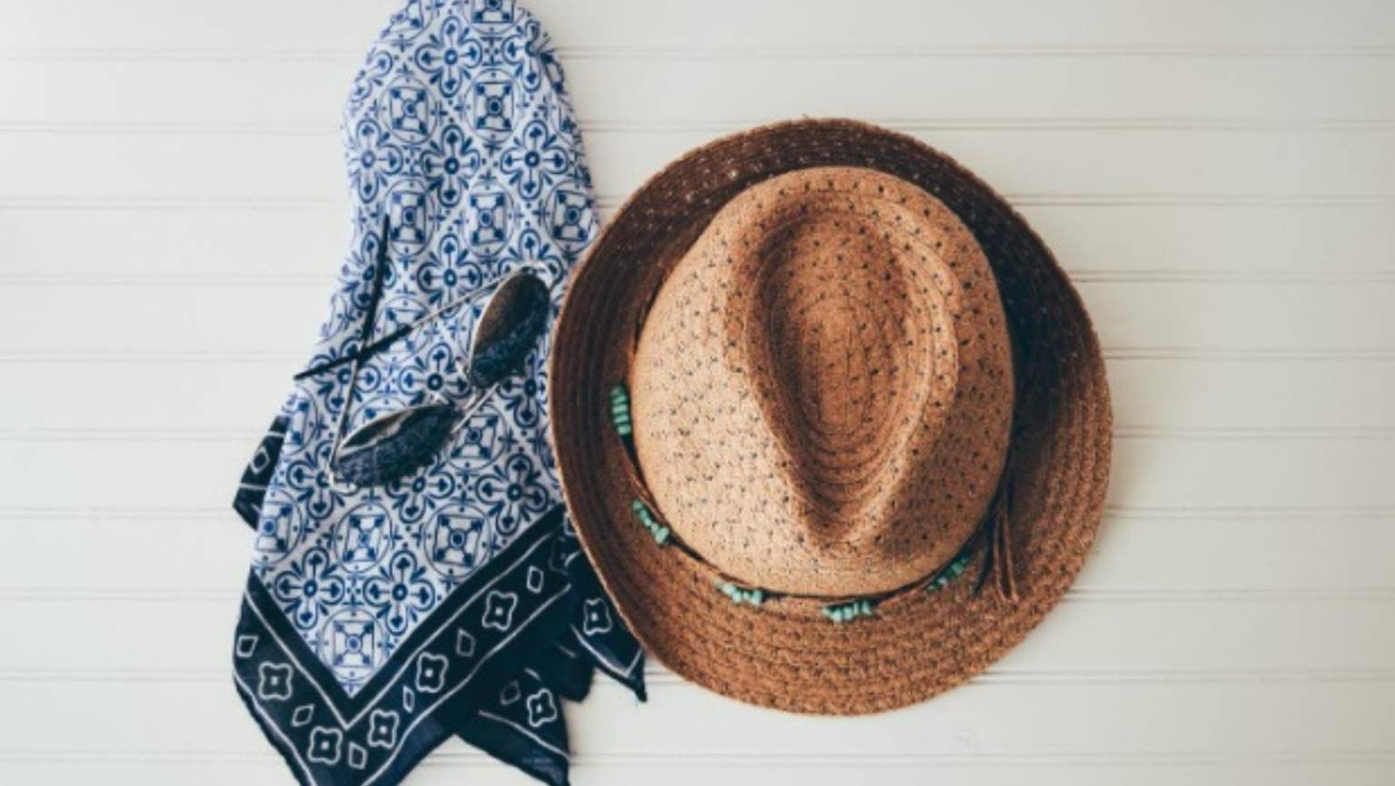 Top down image of straw hat and blue scarf on light grey table