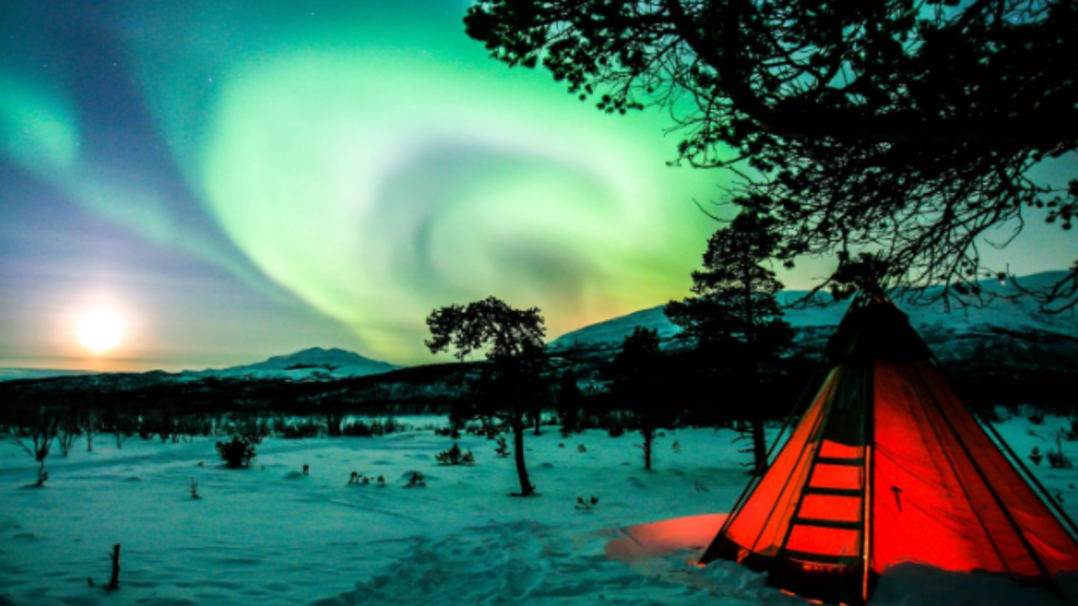 Red tent winter camping with Northern Lights in the sky