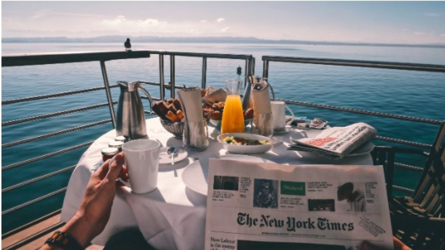 Person reading a newspaper with breakfast food at the bow of a boat